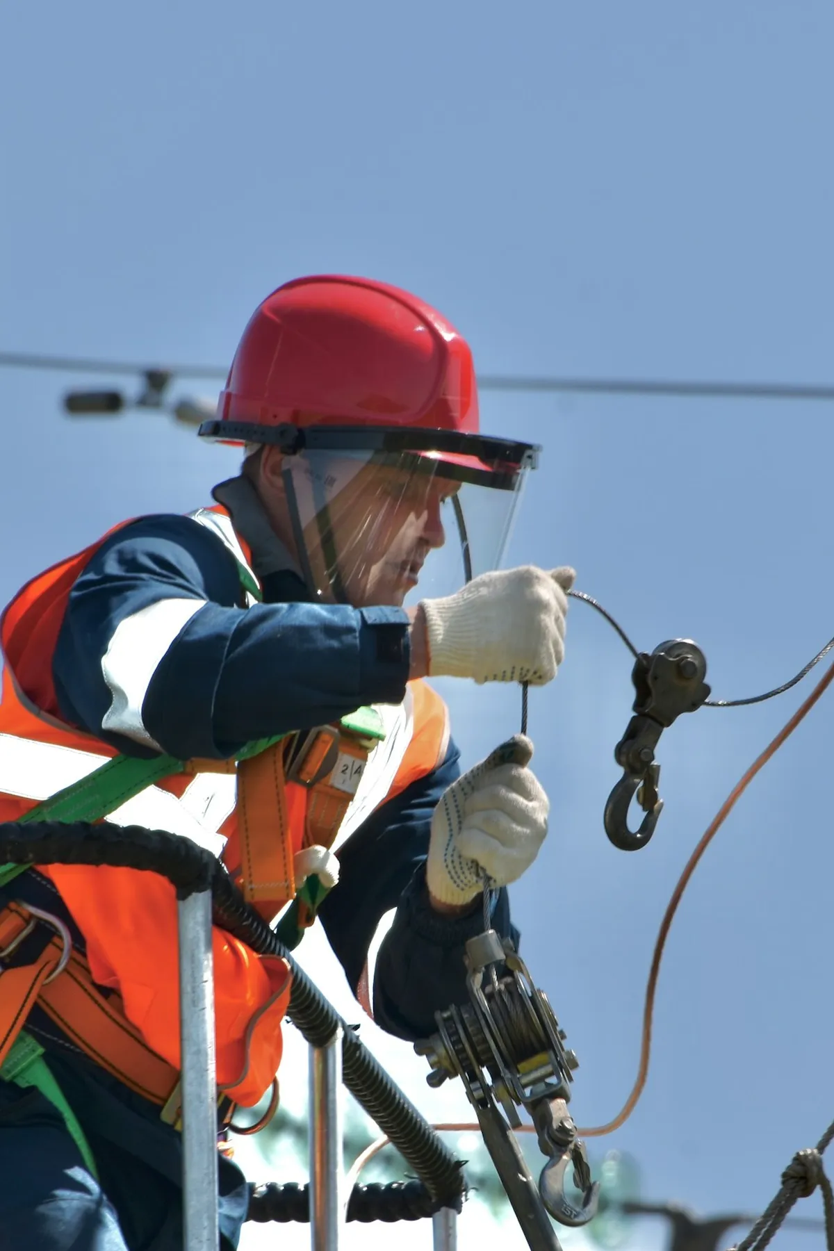 Electrical technician in helmet, face shield and safety harness working on power lines